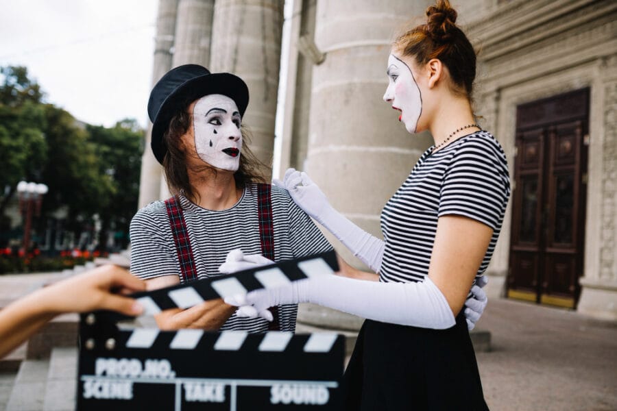 Human hand holding clapperboard in front of surprised female mime looking at male mime